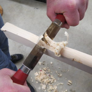 The model uses the Mora push knife to clean up curls left at the bottom of a curve. With the push knife, you can work the wood in an opposite direction without repositioning the piece.
