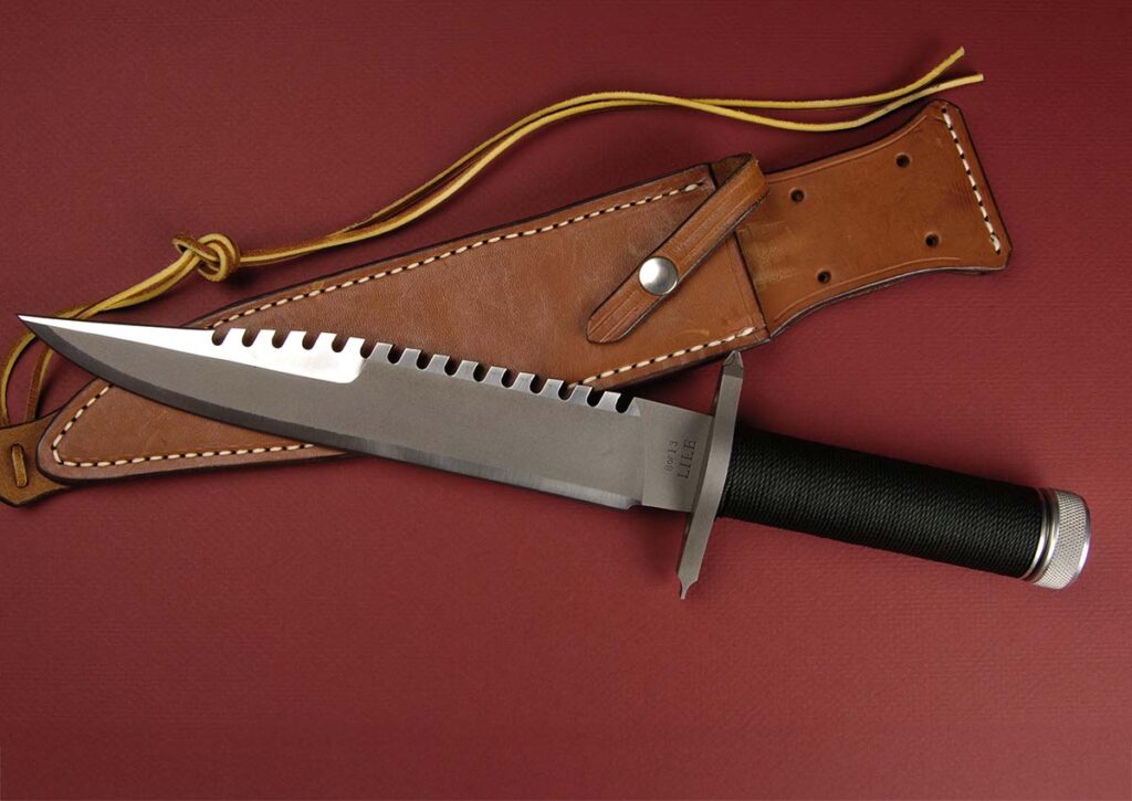 The Sly II, aka the original Jimmy Lile First Blood knife, is the knife that got the author started on his career of buying and selling custom knives 41 years ago. The 9-inch sawtooth blade is bead-blasted D2 tool steel. The hollow handle is cord wrapped with an aircraft-grade aluminum buttcap. Overall length: 14 inches. The leather sheath is custom made. The author’s collector value for one of the originals: $4,000-$6,000.