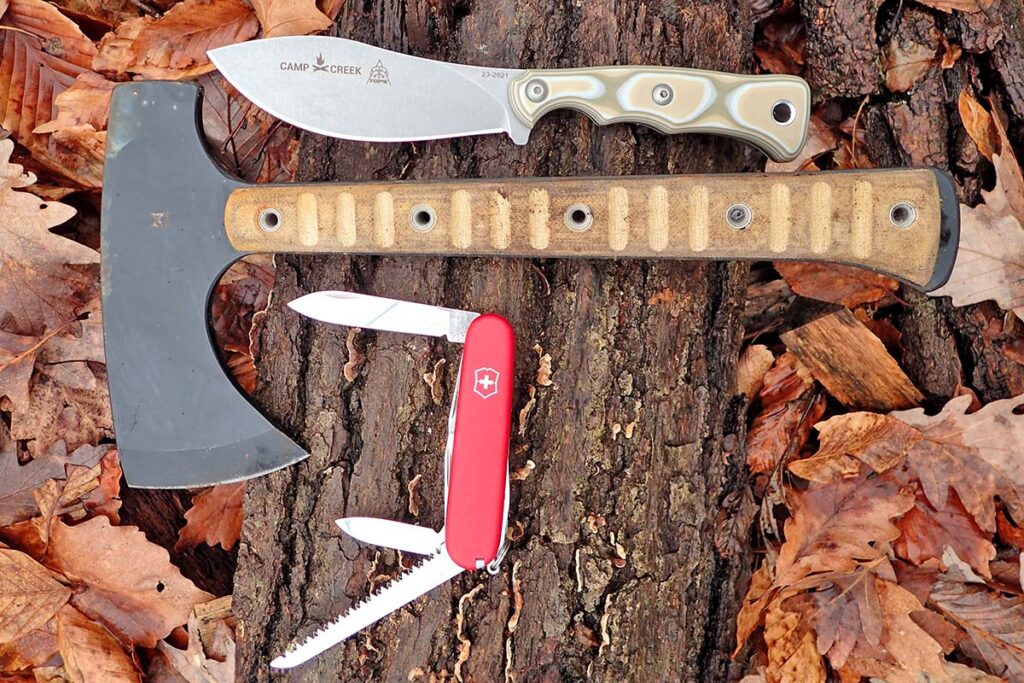 A modern “Nessmuk Trinity” with a Helm Forge hatchet, Victorinox camper, and TOPS Knives Camp Creek.