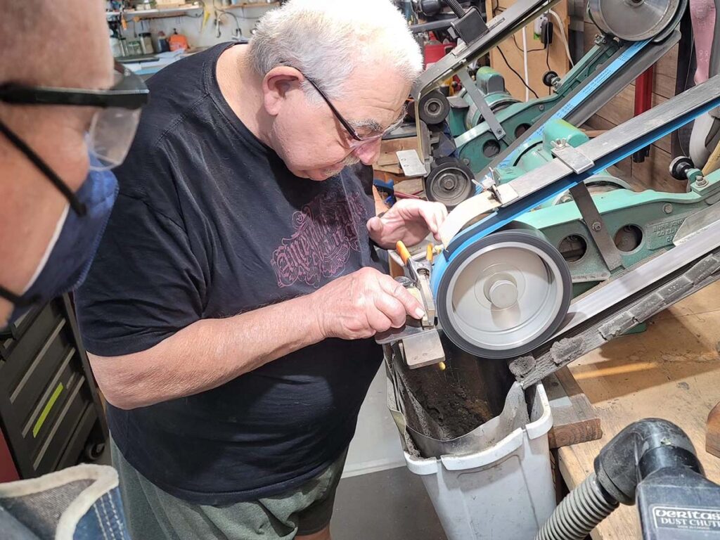 Doing things by hand takes time, especially when you start trying to extend your boundaries. BLADE Magazine Cutlery Hall-of-Fame® member Bob Terzuola has been extending his boundaries a long time, including at the belt grinder. Collector Chris Schluter watches at left.