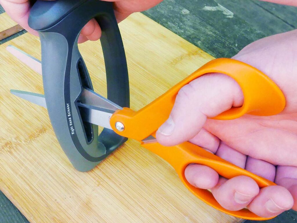 The bevels are sharpened when pushing the scissors blade tips simultaneously into the respective V-slots of the Smith’s unit. The diagonally mounted ceramic rod sharpens both blades at the same time. (Covert image)