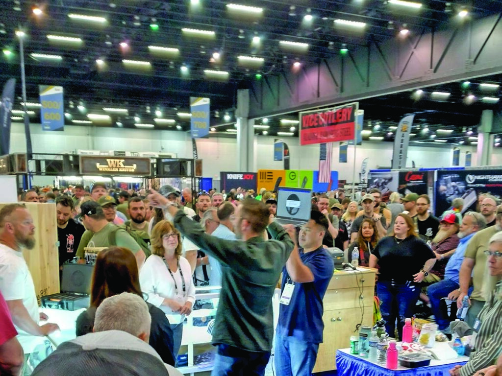 Tim Reeve (center with arms raised) directs traffic at the Chris Reeve Knives booth as Anne Reeve and Dean Felides (directly to Tim’s right) look on.