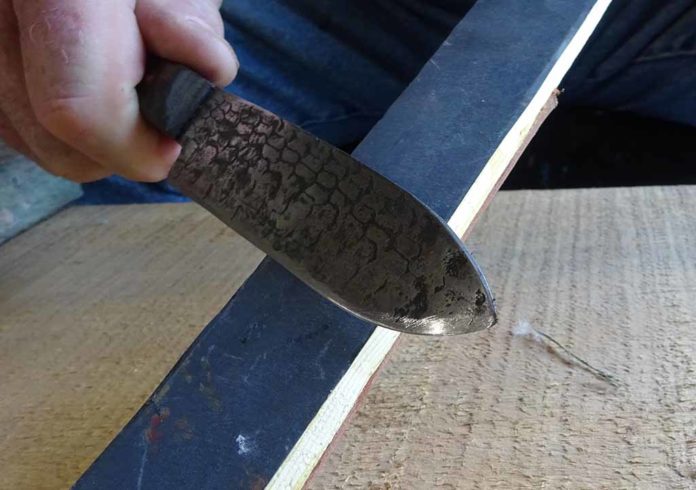 This is the strop on the 1500 grit sandpaper side of the strop stick. The angle is maintained while the smith slides the edge back and forth several times to break the burr. The smith travels the length of the stick and the length of the blade’s edge in a continuous motion.