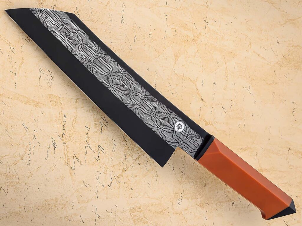The wa handle of Aidan Garrity’s santoku has largely parallel sides to the width of the ricasso with a small ‘beak’ at the bottom for hand retention and aesthetics. Blade steel: mosaic damascus. Vintage butterscotch Micarta® scales boast flat-shield cross-sections and G-10 spacers. Overall length: 14 inches. His list price for a similar knife: $2,300. Its sister piece is a Garrity nakiri that was featured on the March 2024 BLADE® cover. (SharpByCoop image)