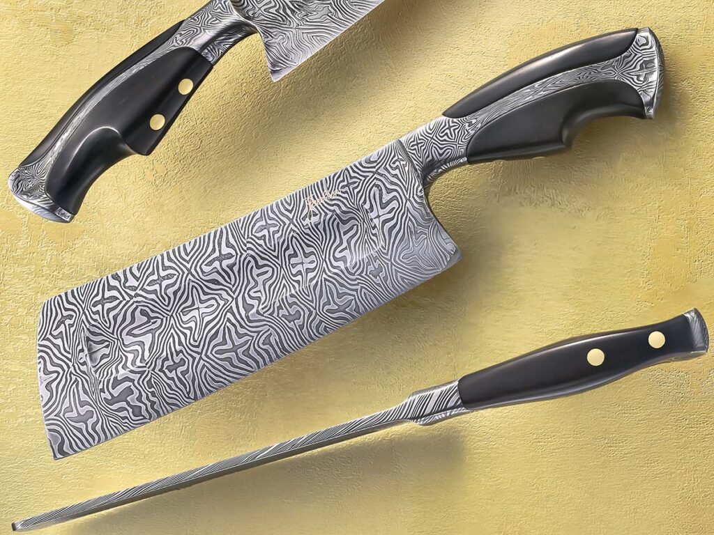 Having served time in professional food service, practical utility is never far from David Jacobson’s mind. However, he isn’t afraid of adding some flourish to his creations, such as the gold-inlay signature near the spine of his mosaic damascus bladed and ebony scaled cleaver. (SharpByCoop image)